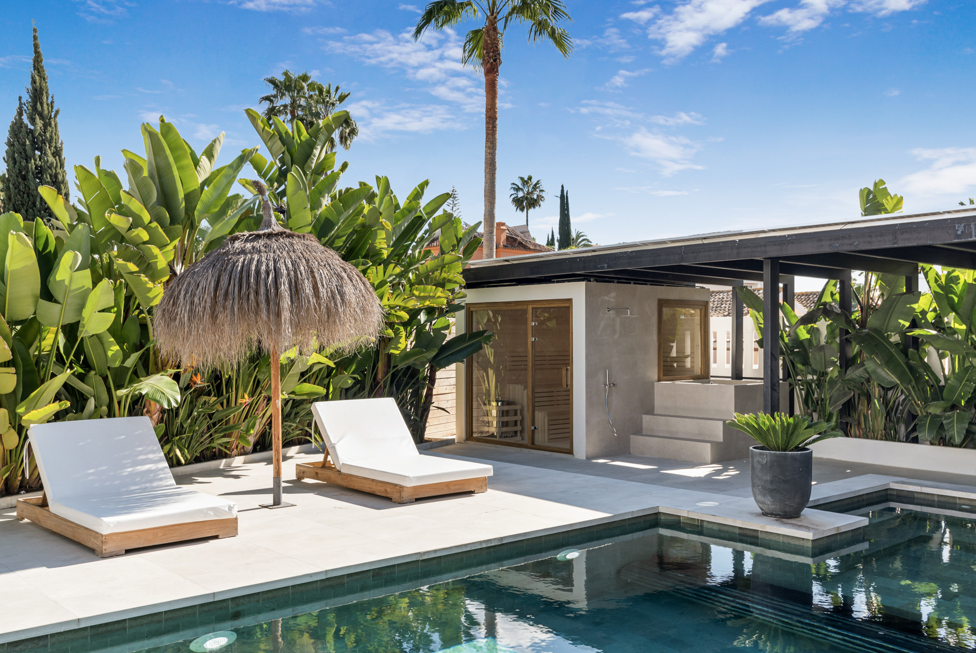 Close-up of the pool area showcasing loungers, a shower, and lush plants around the pool.