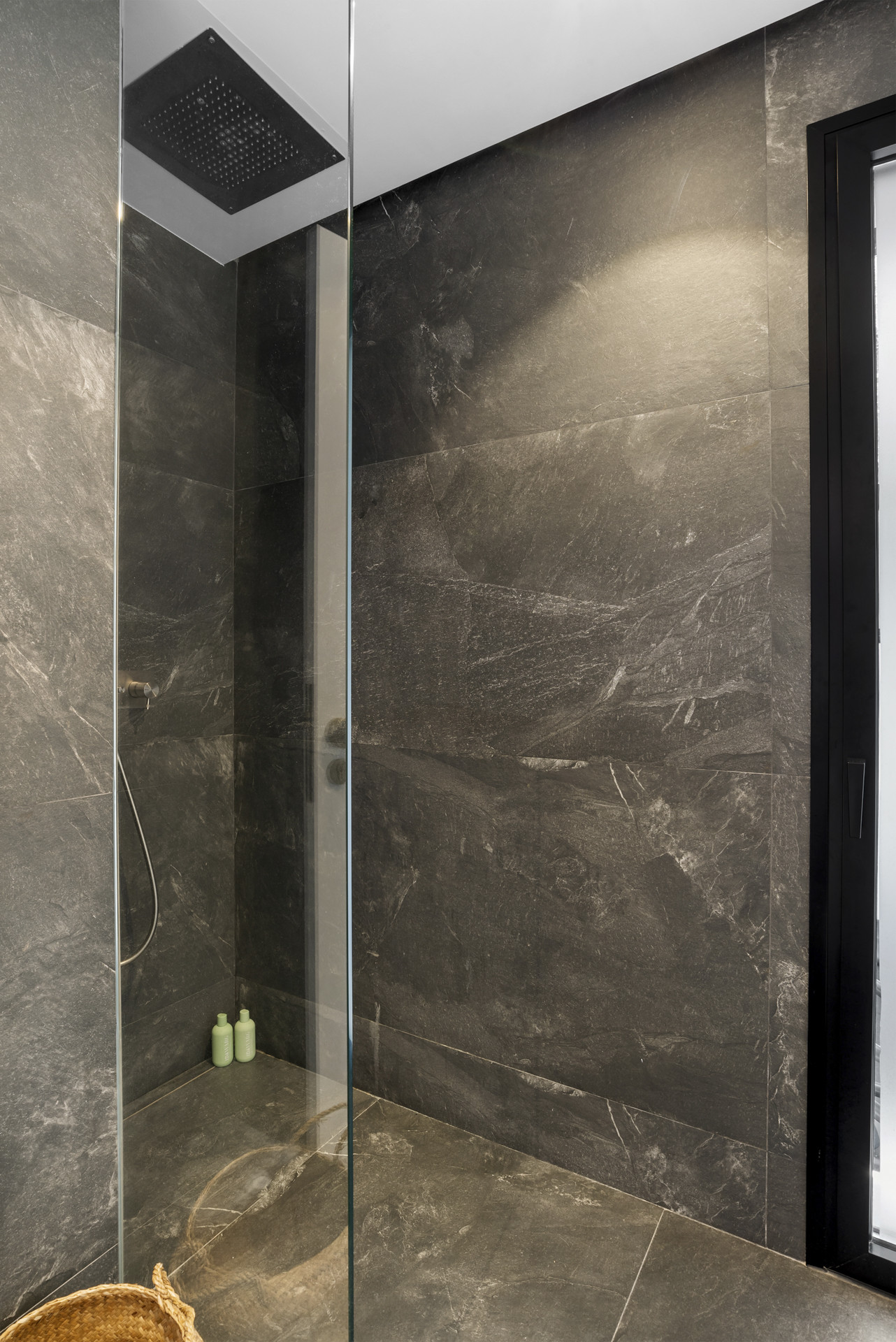 Shower space with dark tiles and glass partition.