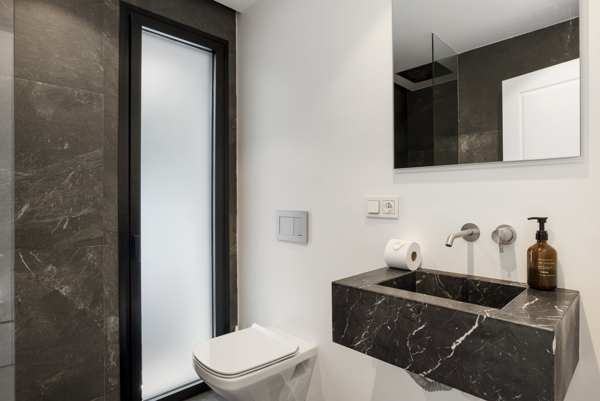 Minimalist bathroom with dark marble and modern fixtures.