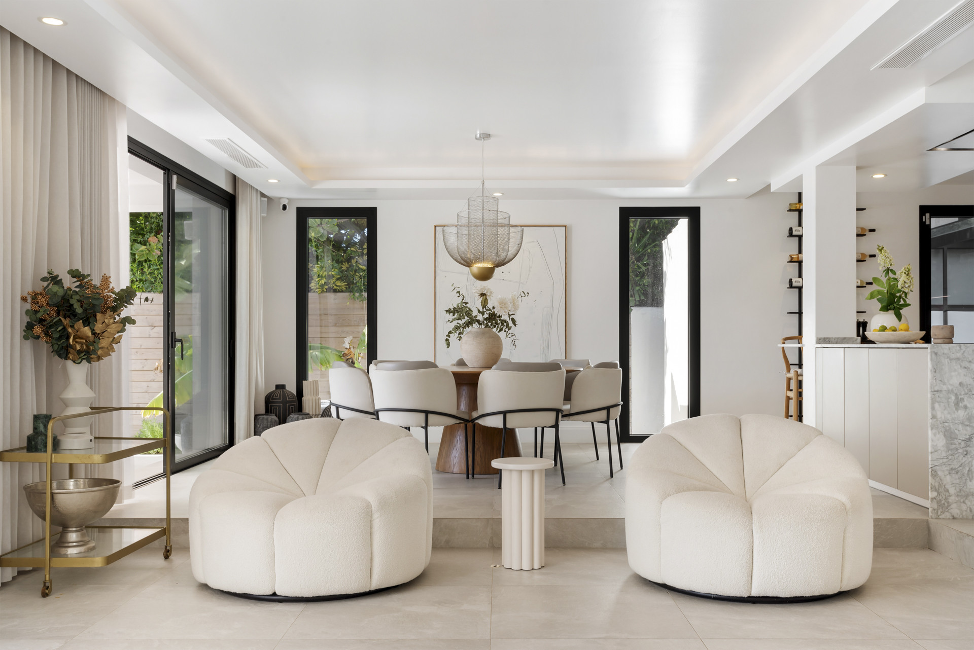 Stylish dining area with a round table, modern chandelier, and plush seating next to large windows.
