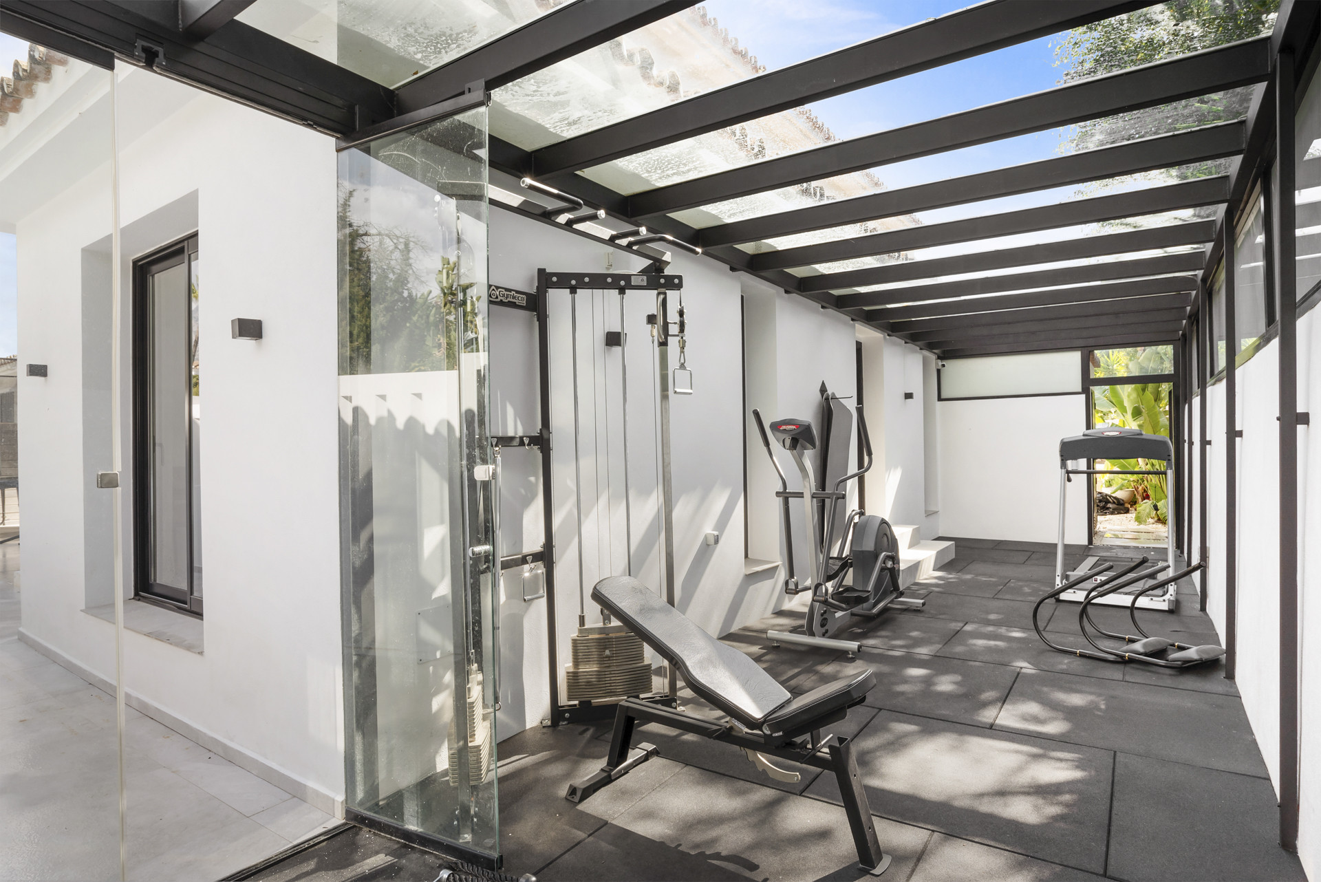 Indoor gym featuring exercise machines under a glass roof.