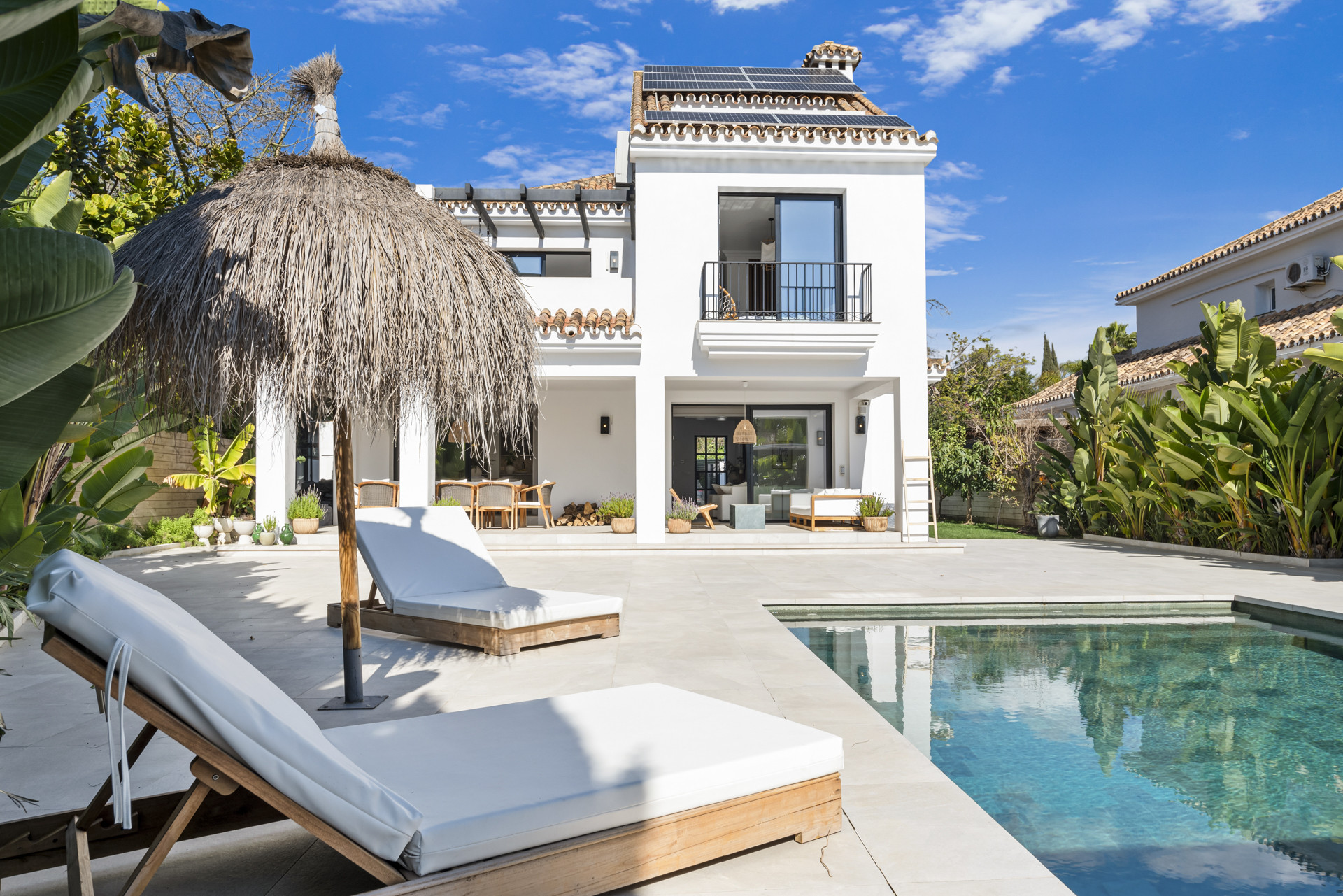 Back view of the villa featuring a pool, loungers, and outdoor seating with greenery.