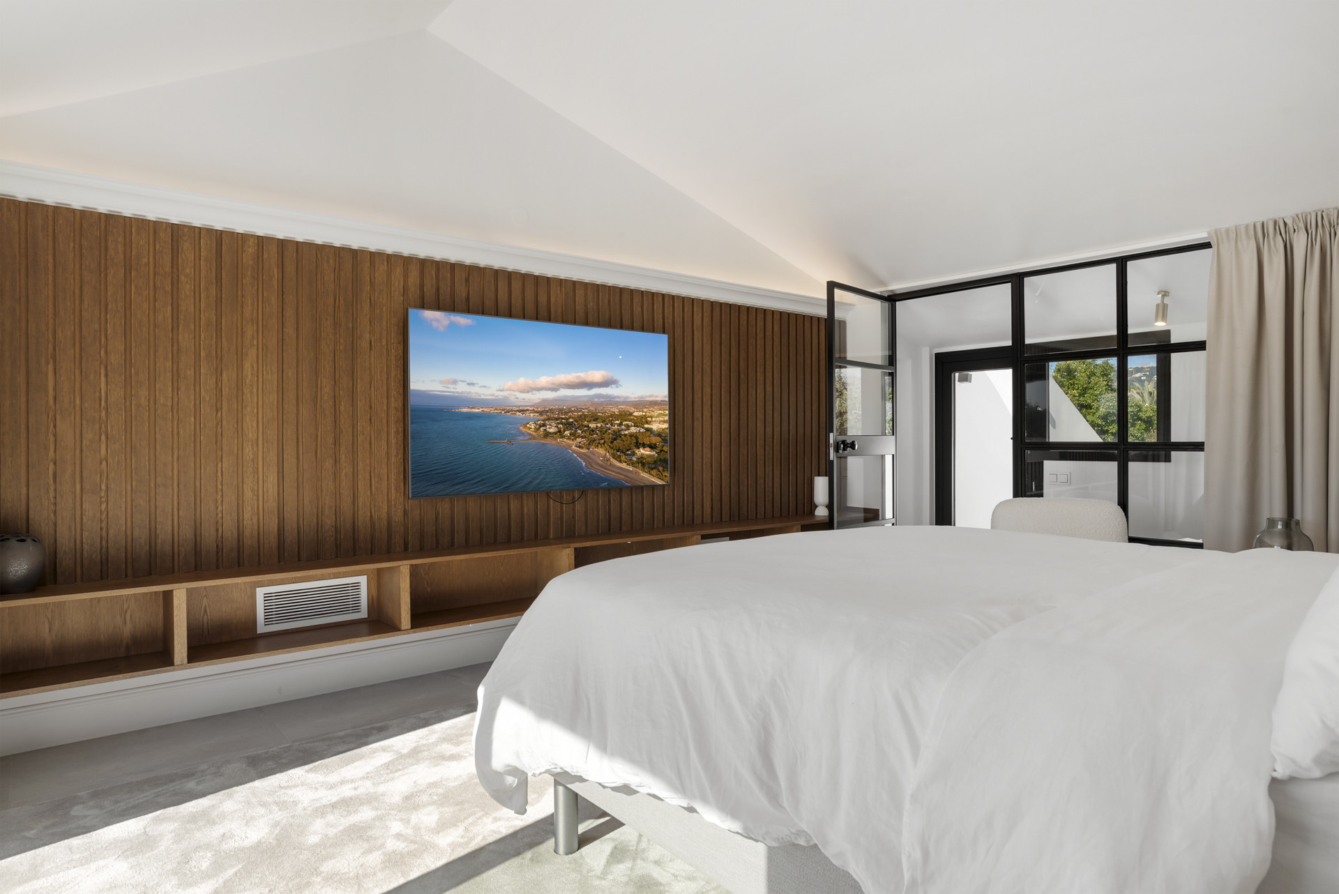 Room with wood accent wall, large TV, and view of outdoor area through glass doors.