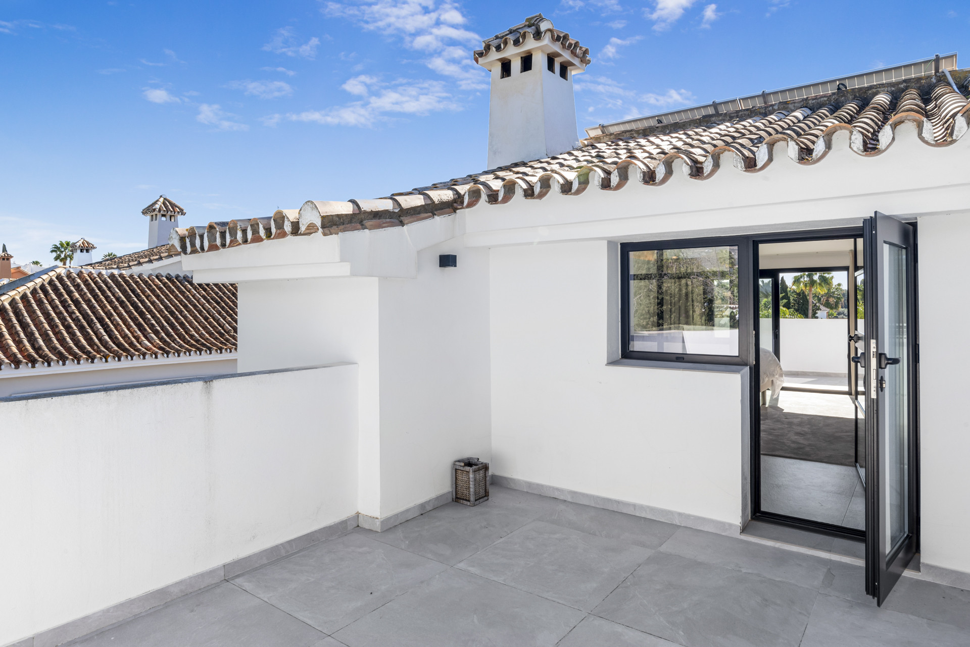 Rooftop terrace showing a tiled roof, open doors, and views overlooking the garden and nearby structures.