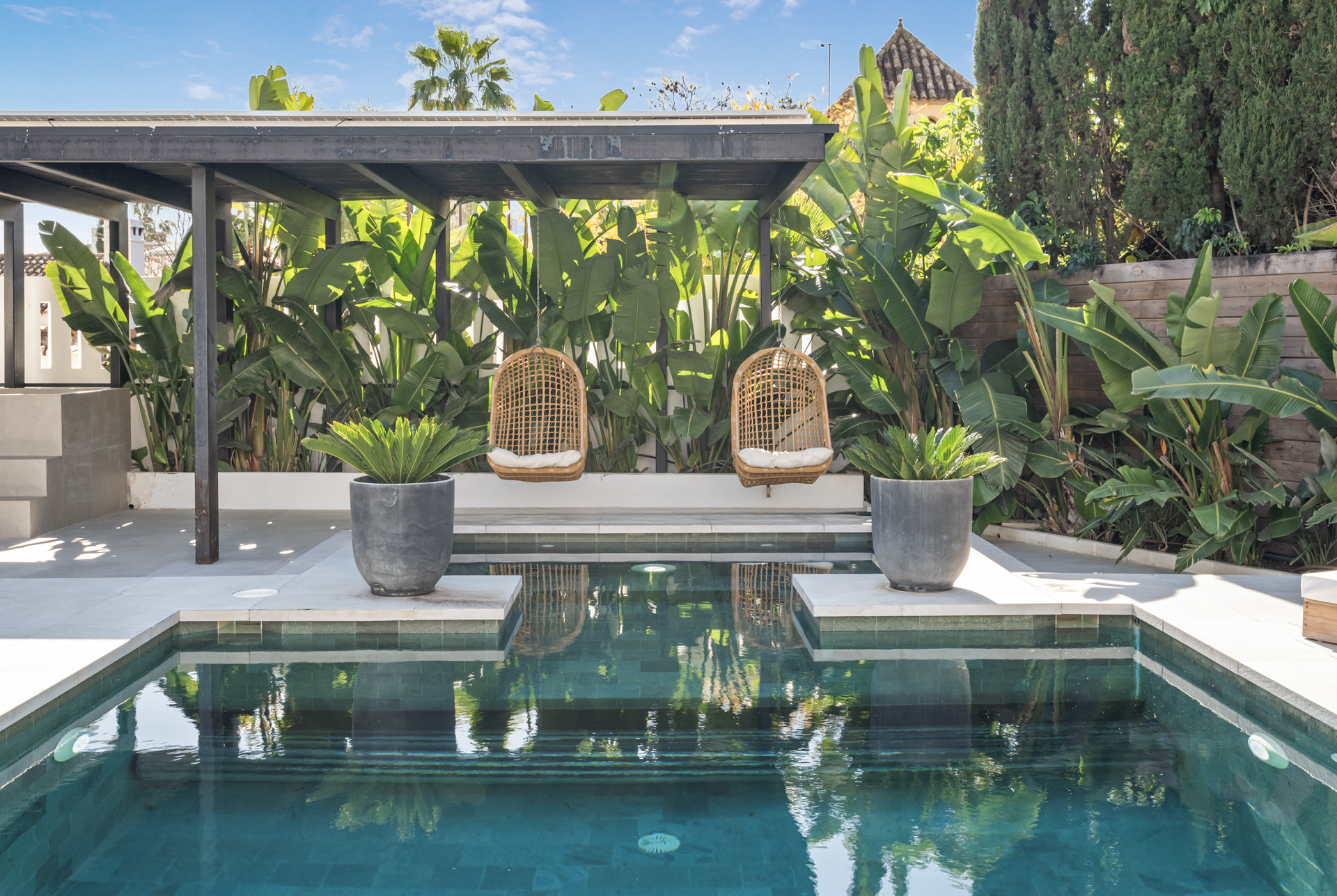 Insight into the pool area with hanging chairs and planters near the water.