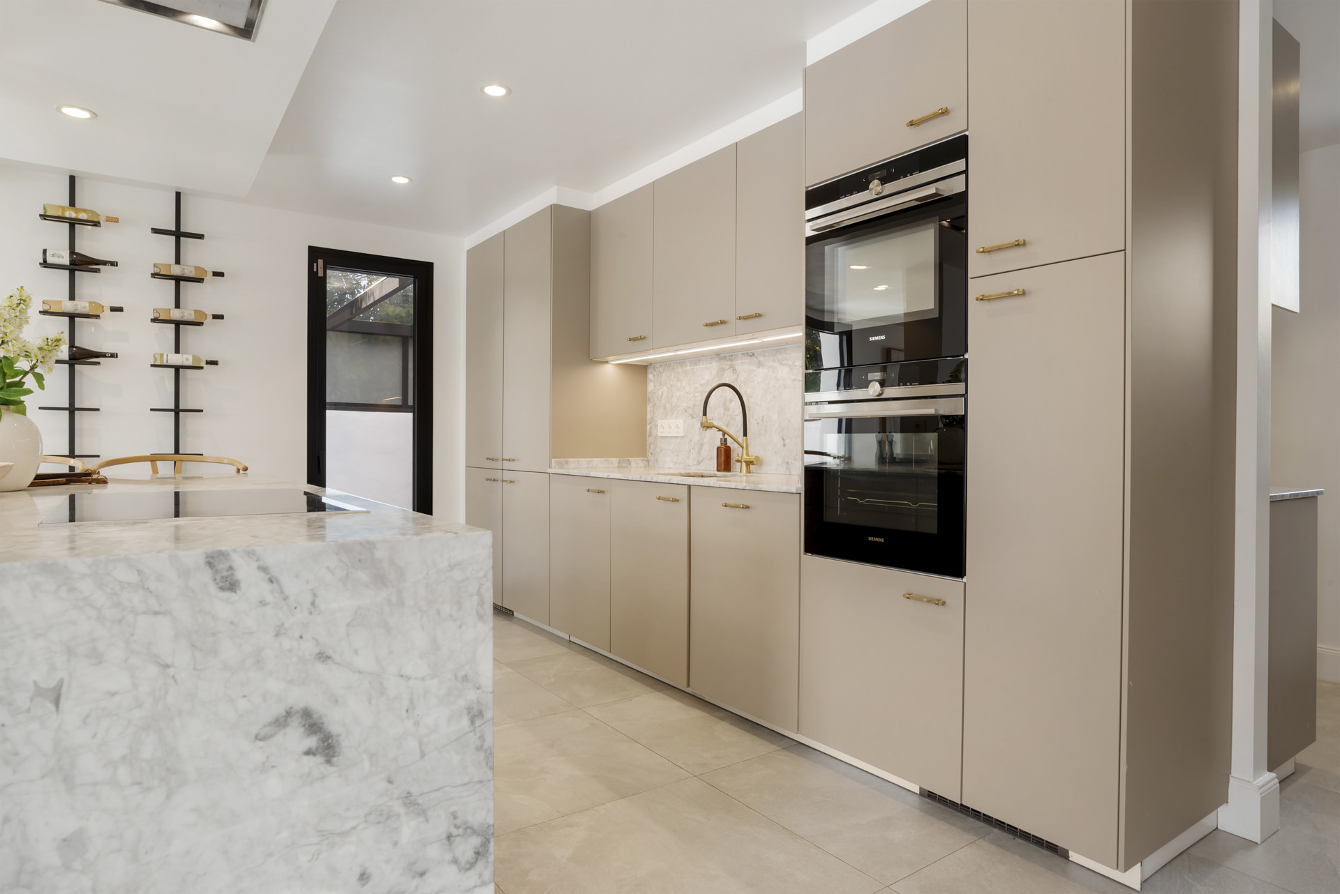 Modern kitchen with marble counter, built-in appliances, and shelving units.