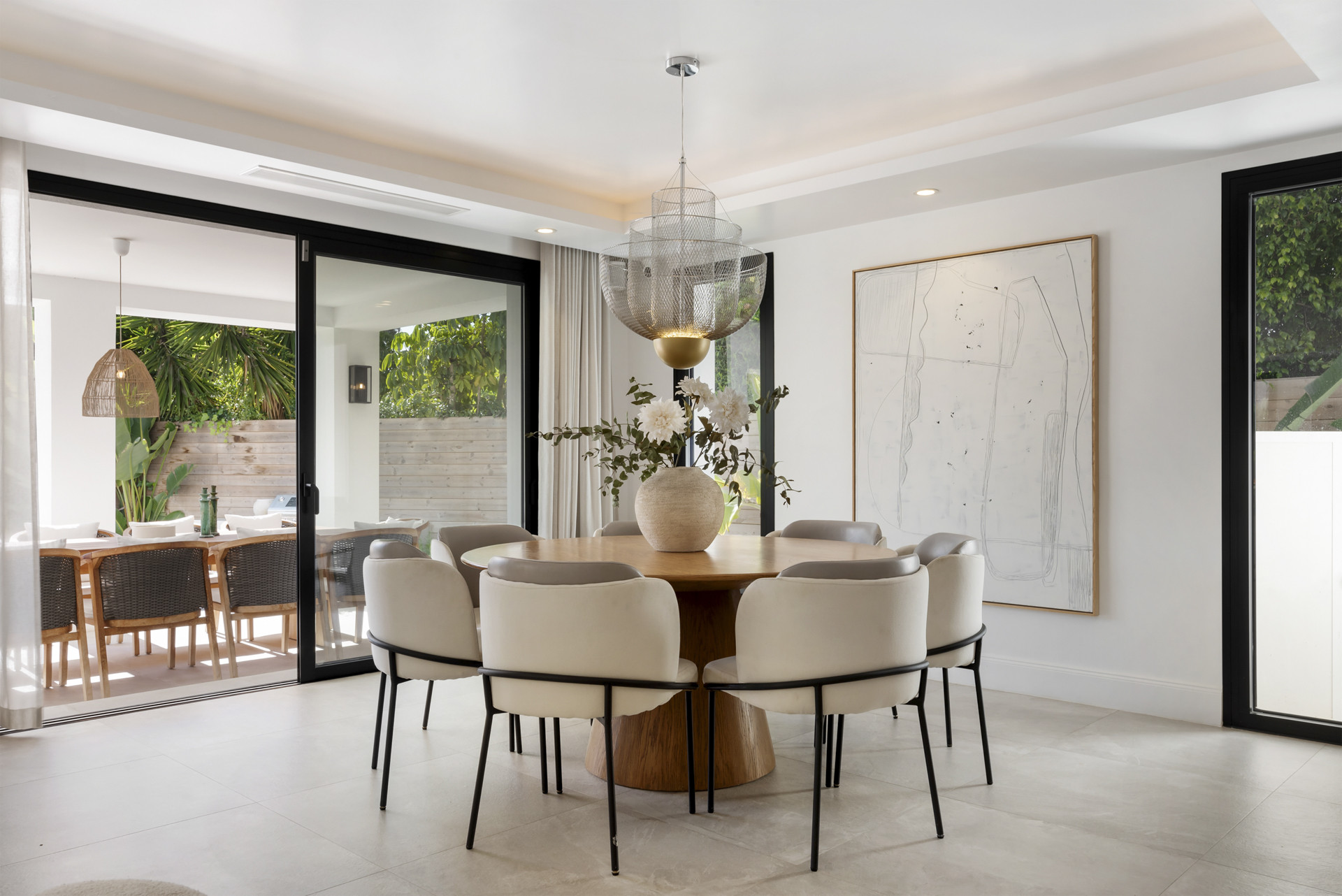 Modern dining table set with neutral chairs, botanical centerpiece, and large sliding doors to the outdoor area.