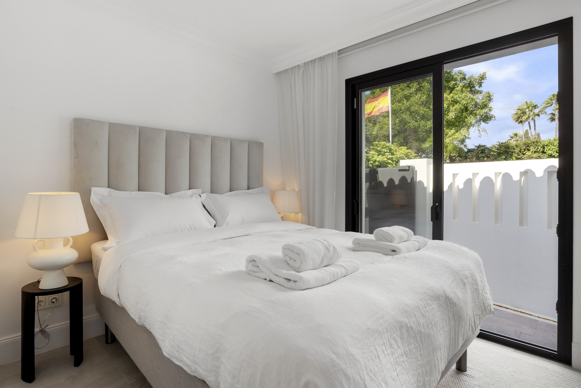 Cozy bedroom with a large bed, light-colored linens, and sliding doors to a garden.