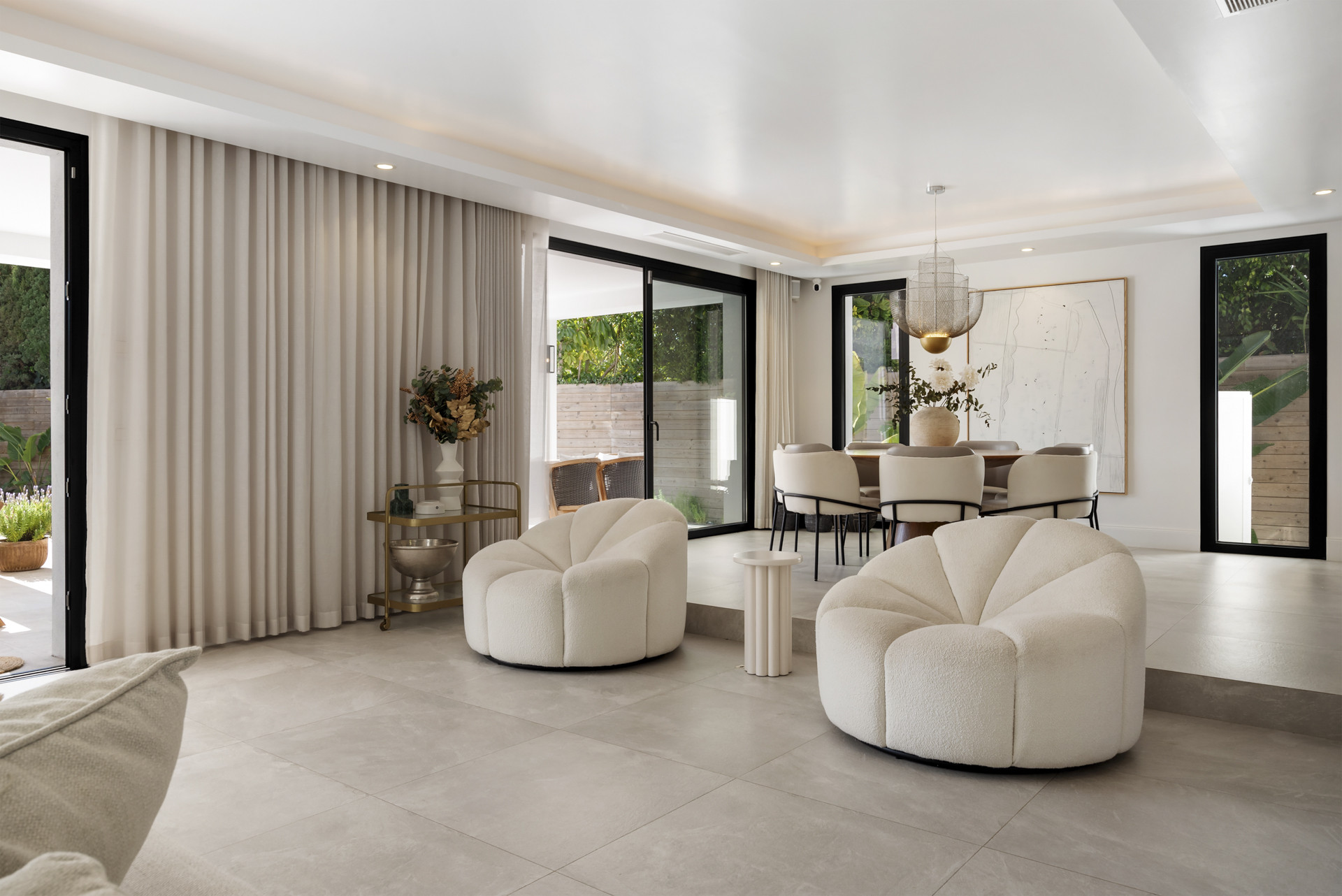 Seating area with soft chairs, a coffee table, and an adjacent dining room showcased through big glass doors.