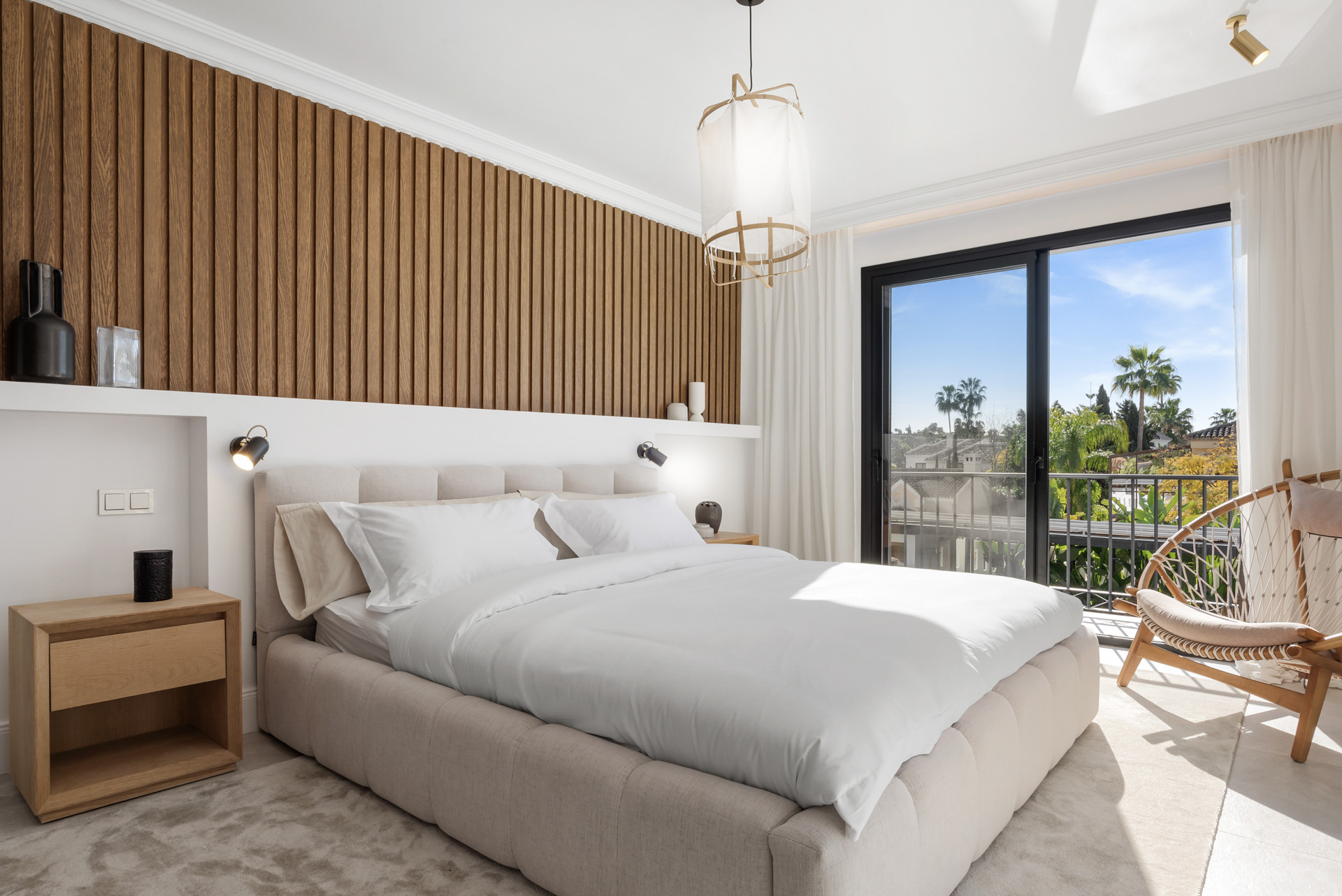 Master bedroom with wood-paneled wall and large window overlooking greenery.