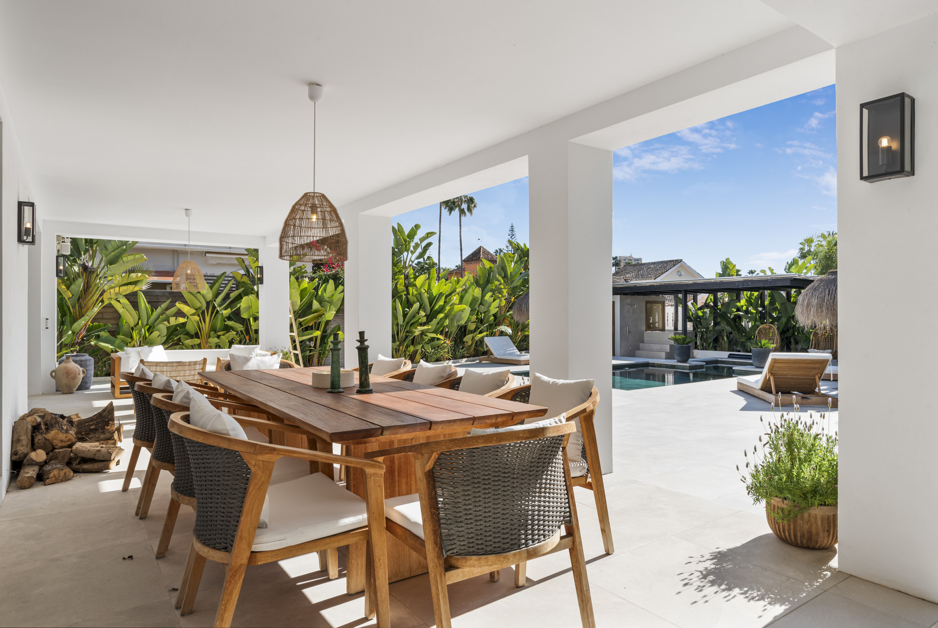 Open terrace dining area with large table and view of lush greenery and pool.