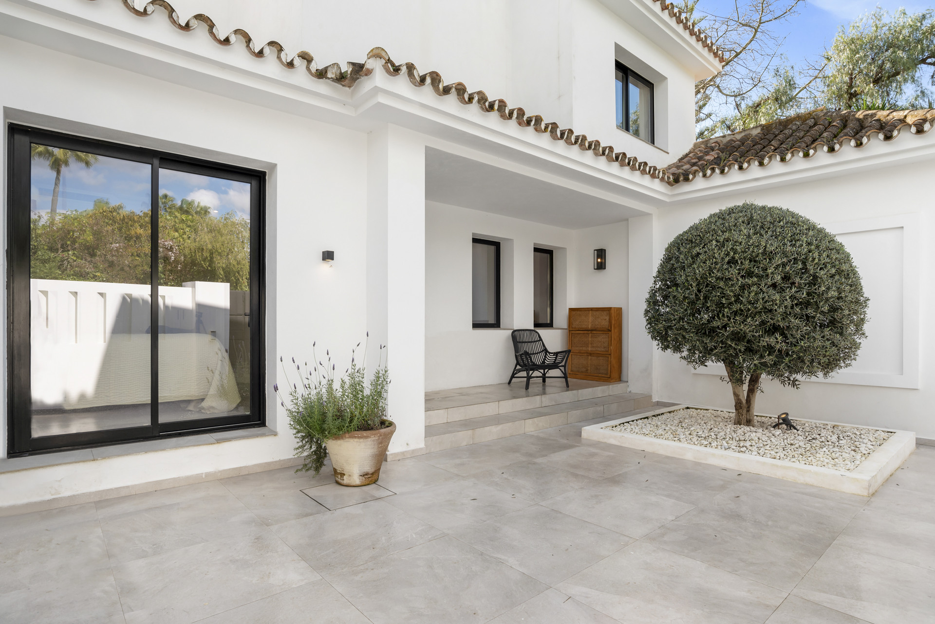 Entrance area with a paver stone floor and trimmed bushes in pots.
