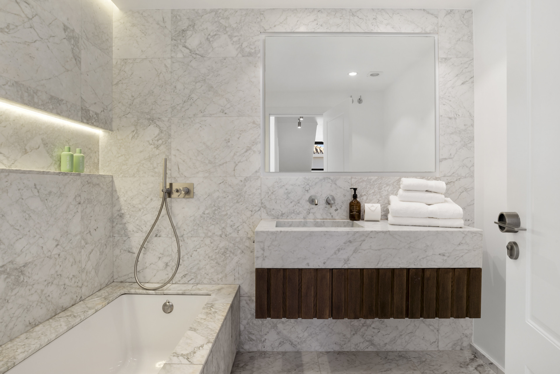 Modern bathroom with marble walls, tub, and sleek sink area.