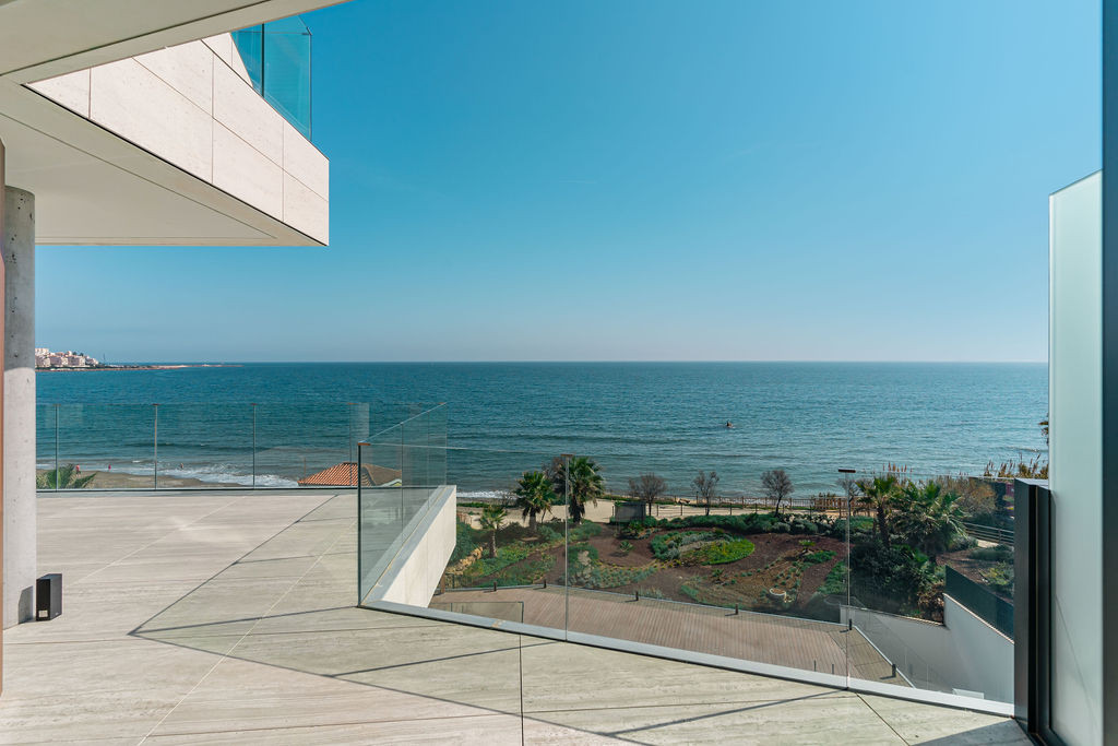 Corner of a balcony with glass railing, stone flooring, and expansive views of the blue sea.