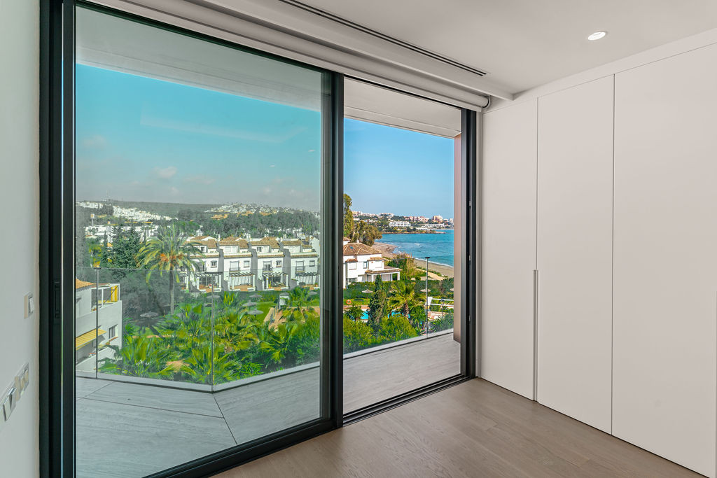 Bedroom with ocean view through sliding glass doors, featuring a built-in white wardrobe.