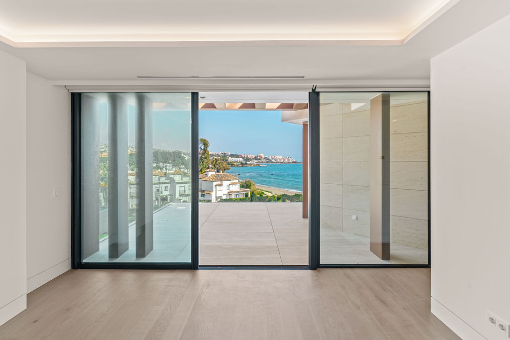 Empty room with floor to ceiling sliding glass doors opening to a terrace with sea views.