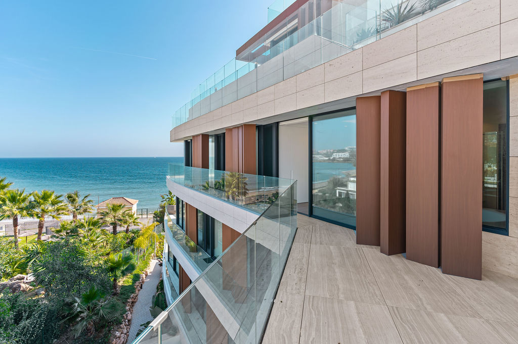 Side view of a building balcony with glass railings and wooden privacy screens, facing the ocean.