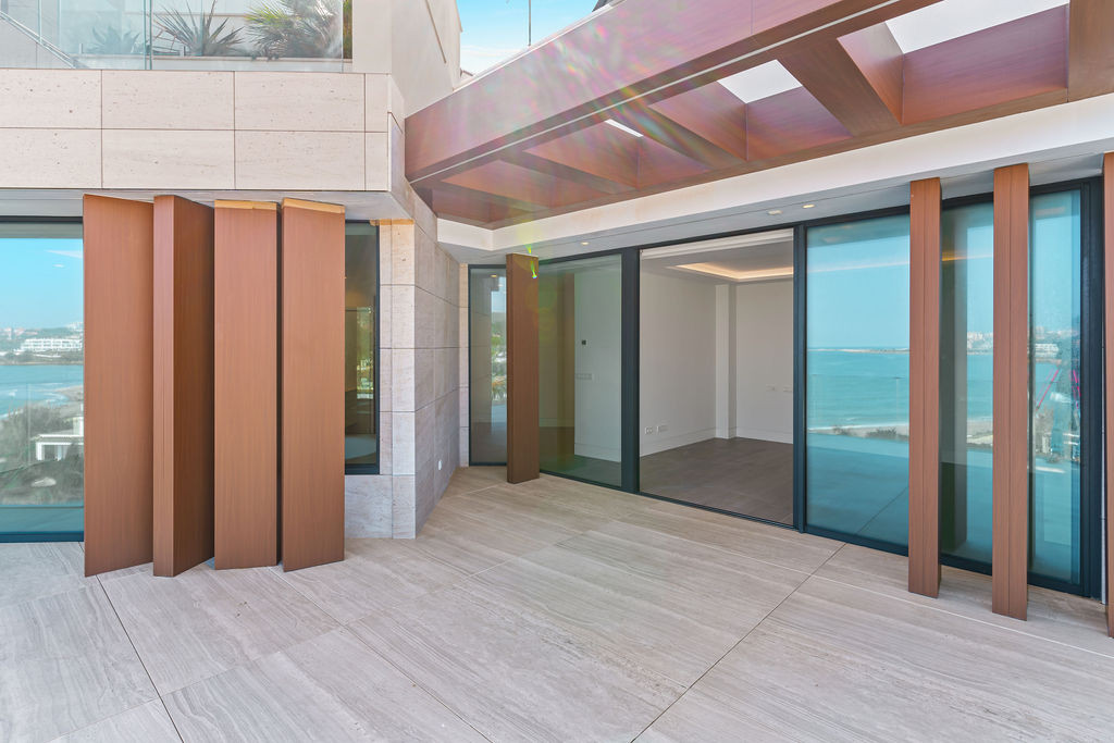Outdoor terrace with large sliding glass doors, wooden accents, and distant sea views.
