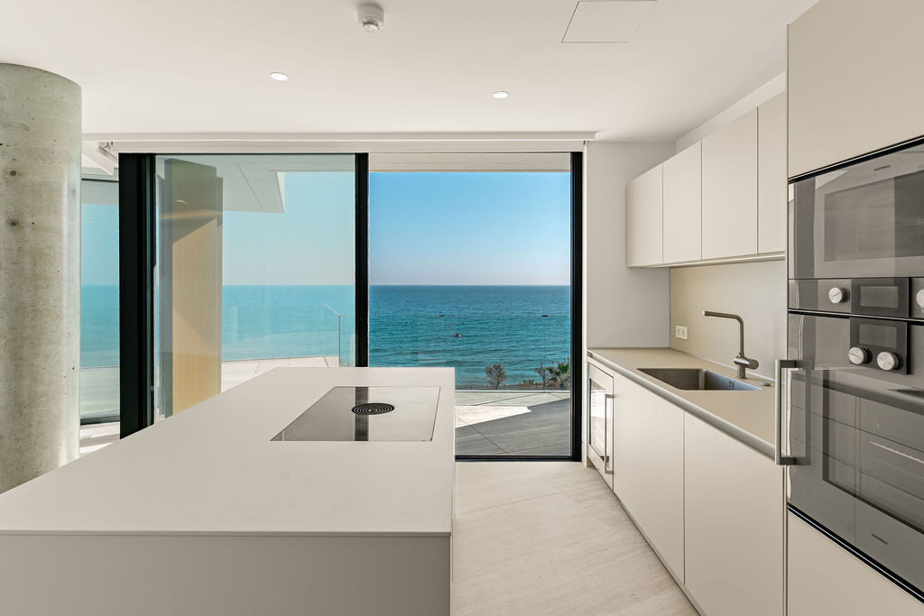 Modern kitchen with a light grey island and appliances, featuring a large ocean view through sliding doors.
