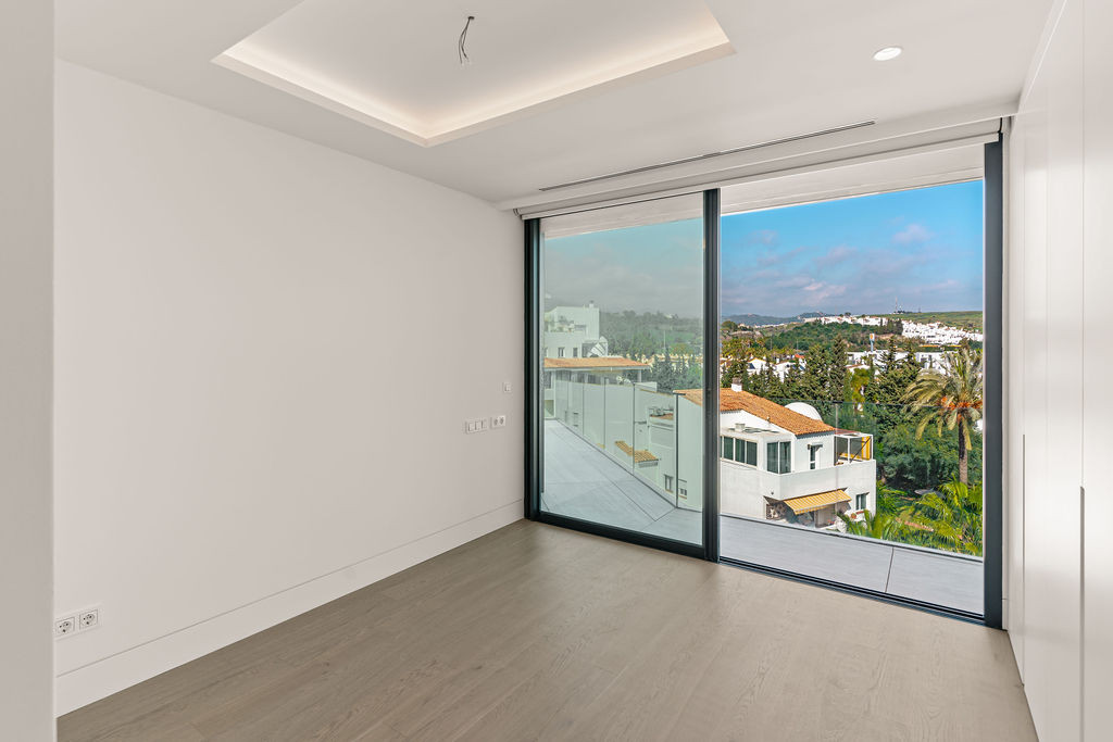 Bedroom with full-height sliding glass doors opening to a scenic view of white buildings and hills.