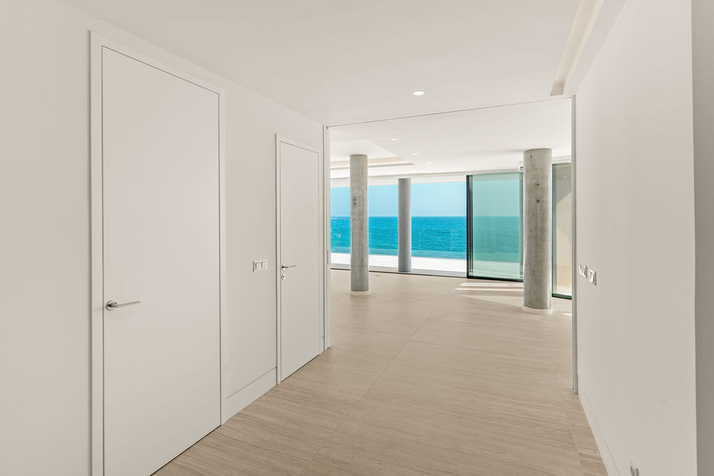 Modern hallway with white doors and light floor tiles leading to a room with ocean views.