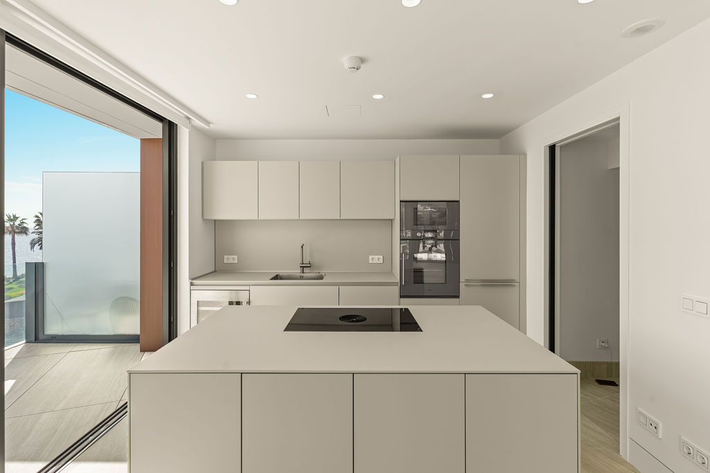 Contemporary kitchen featuring a large island, integrated ovens, and a clear view of the sea from a sliding door.