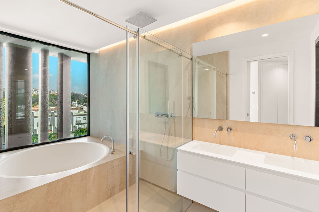 Modern bathroom with a freestanding tub by a window, double vanity, and a glass shower enclosure.