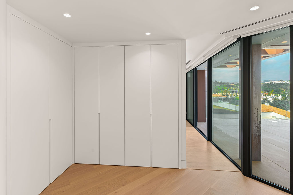 Hallway with light wood flooring, white built-in wardrobes, and expansive glass windows overlooking hills.