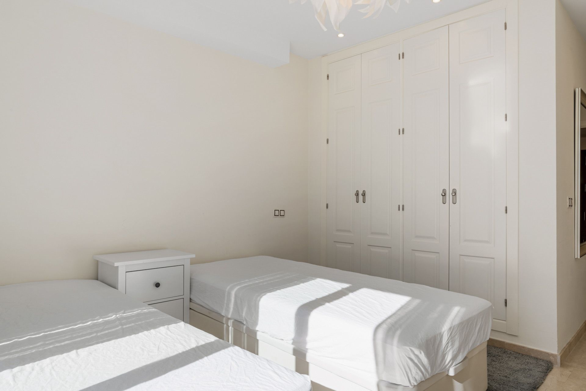 Bedroom featuring two beds, a white nightstand, and a full wall of white built-in wardrobes.
