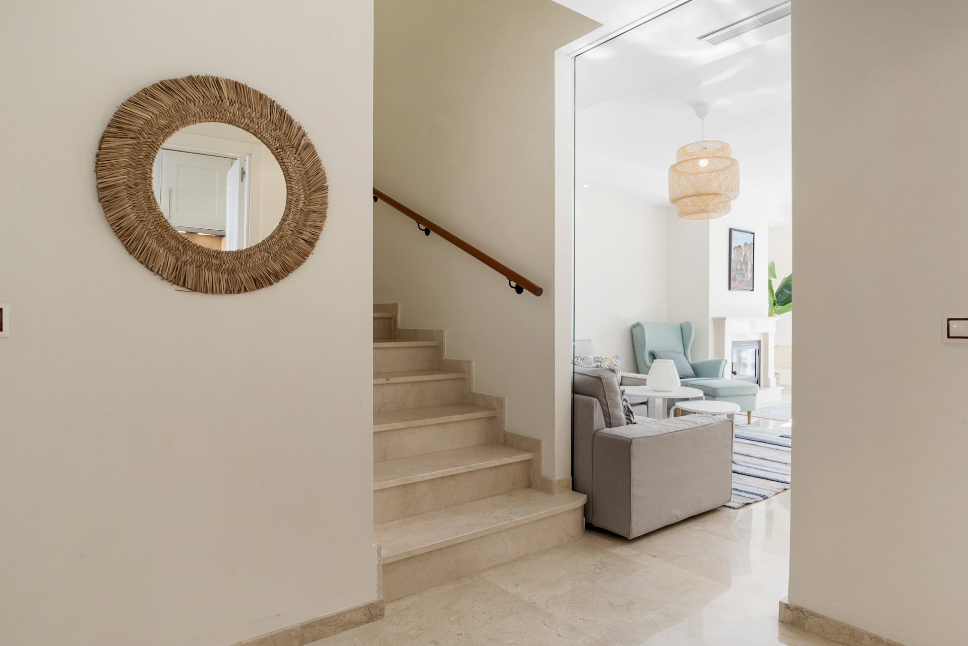 Entryway showing a round woven mirror, marble stairs, and a partial view into a living room.