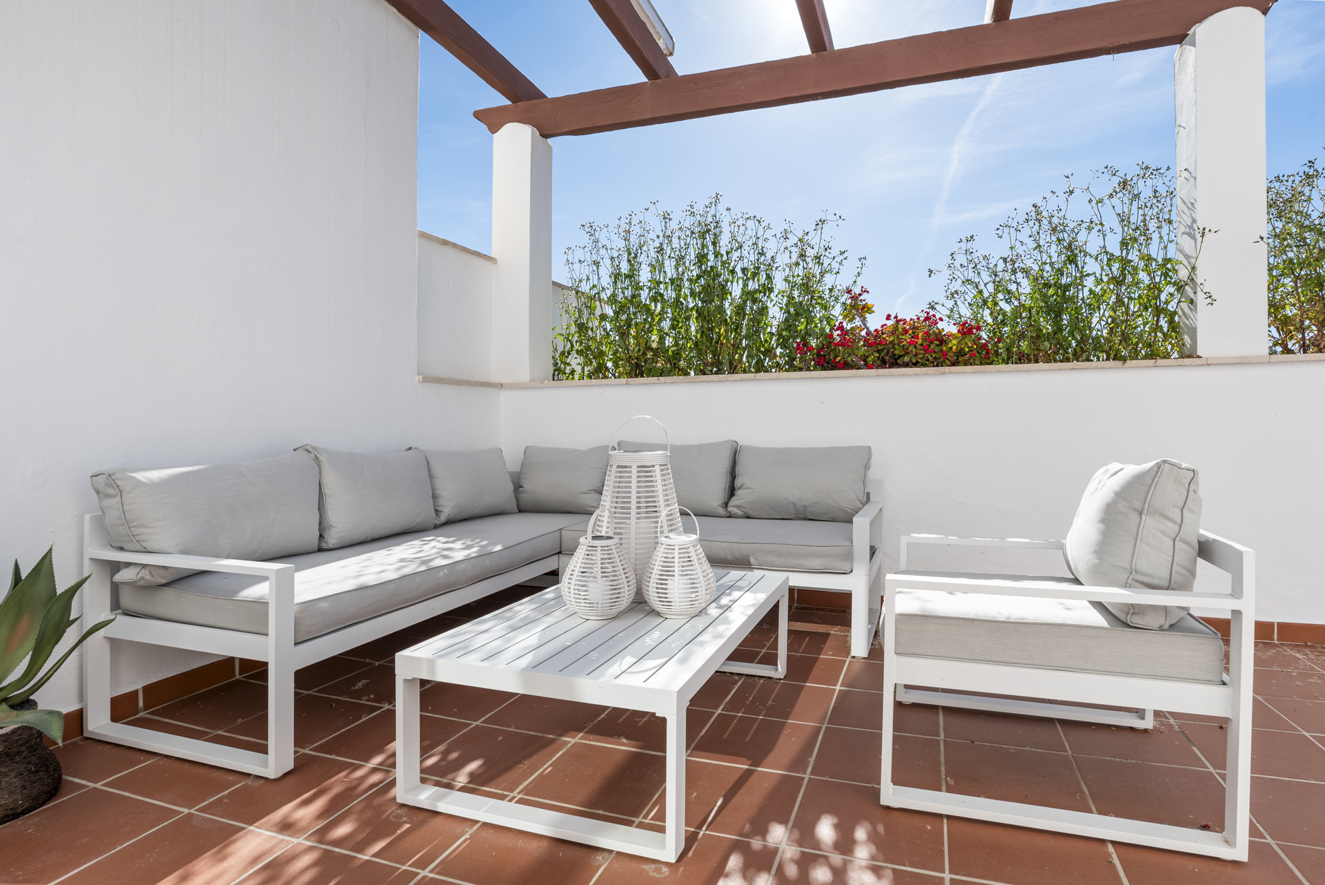 White outdoor sofa and chair set with gray cushions on a sunlit terra cotta terrace.