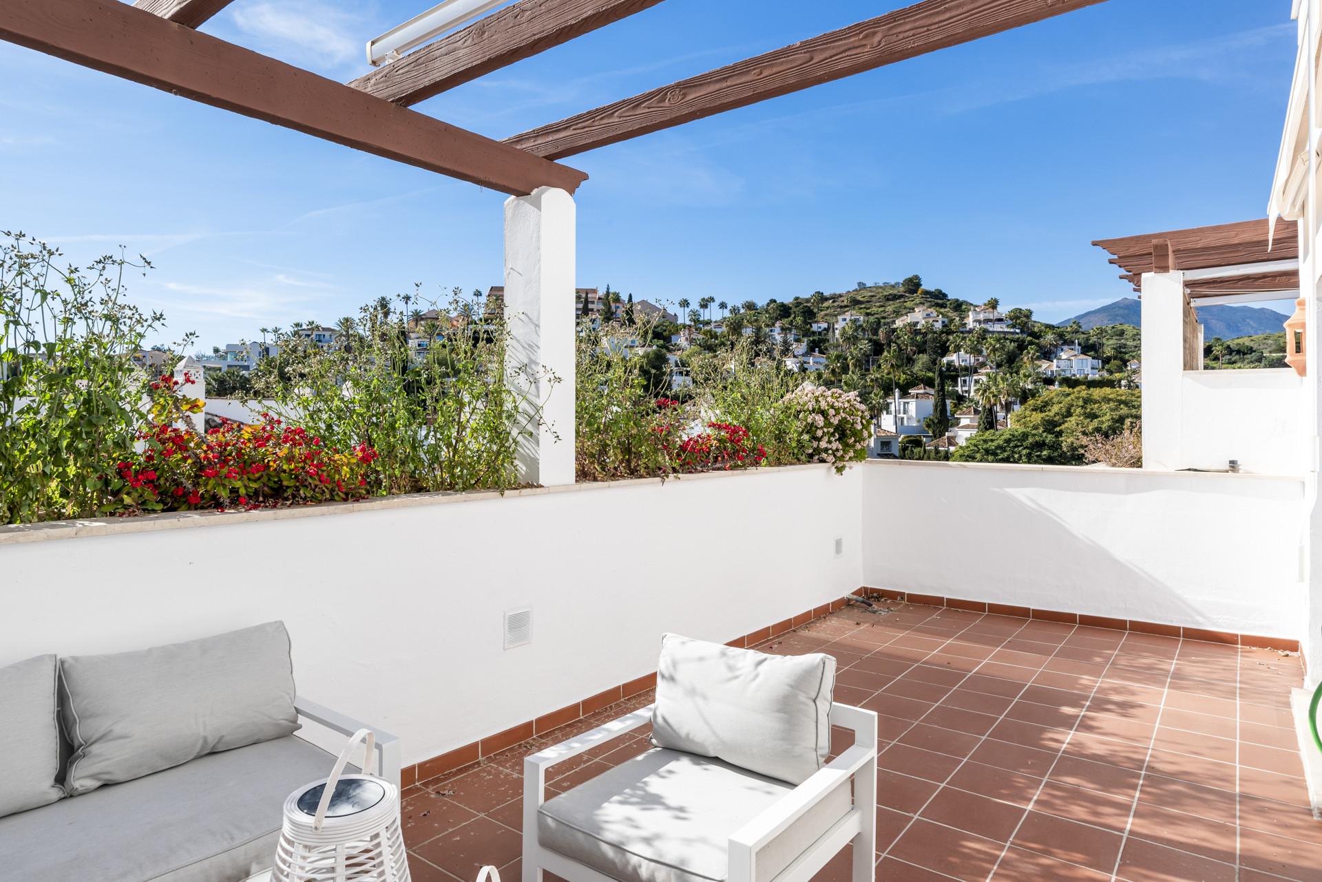 Outdoor lounge chairs on a terra cotta terrace, facing a hillside view with lush plants.