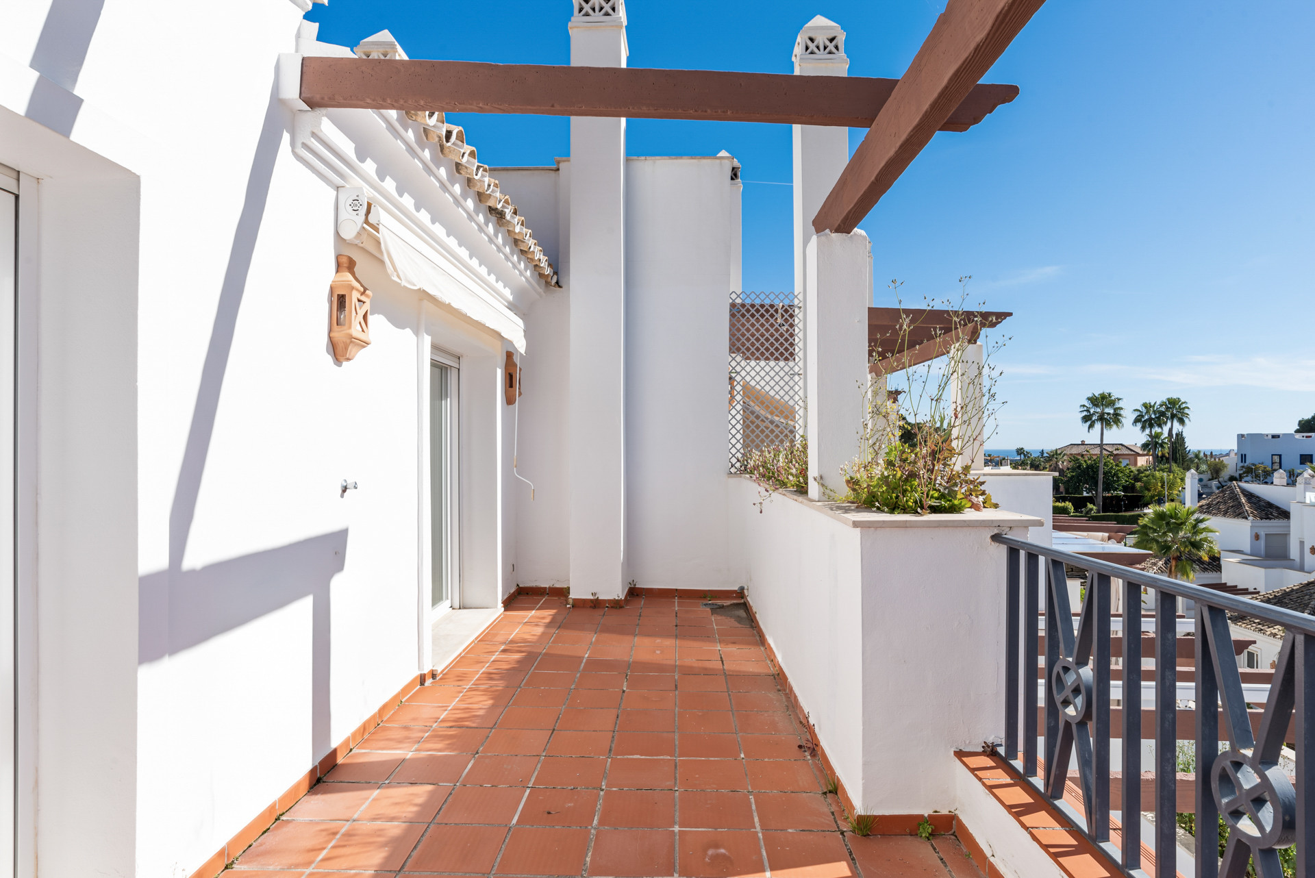Outdoor terrace with terra cotta tiles, white walls, and a wooden pergola structure.