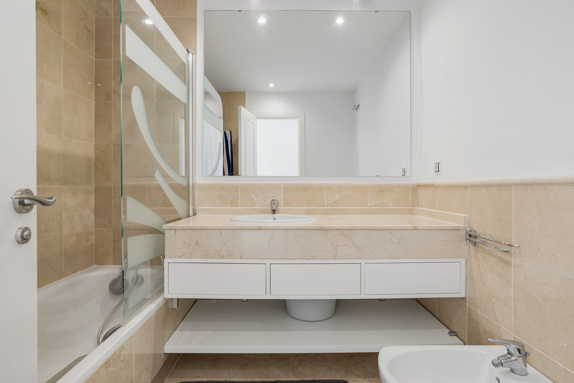 Bathroom with a large mirror, light marble countertop, single sink, bathtub, and bidet.