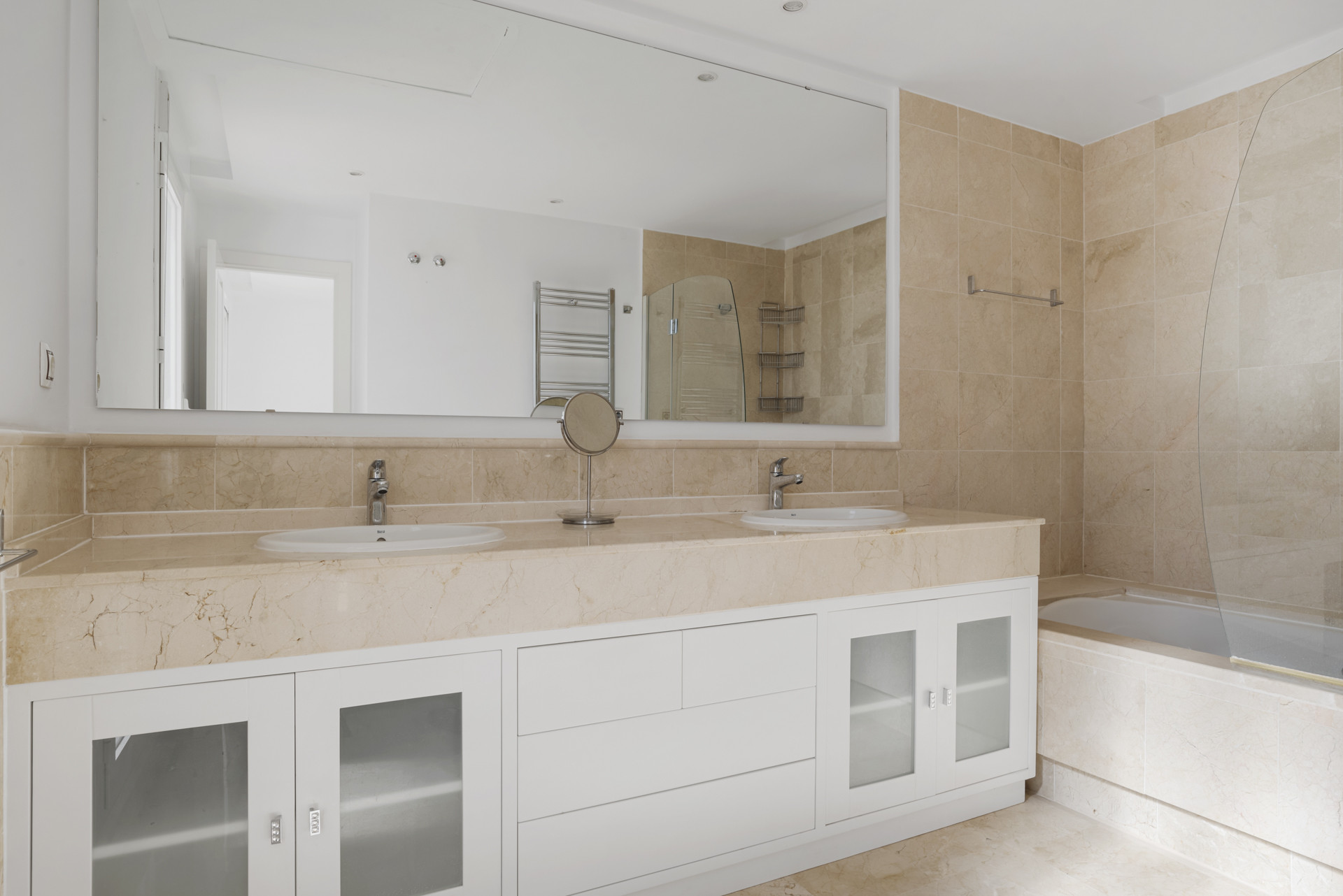 Bathroom with double vanity sinks set in a marble countertop and a large mirror over a built-in tub.