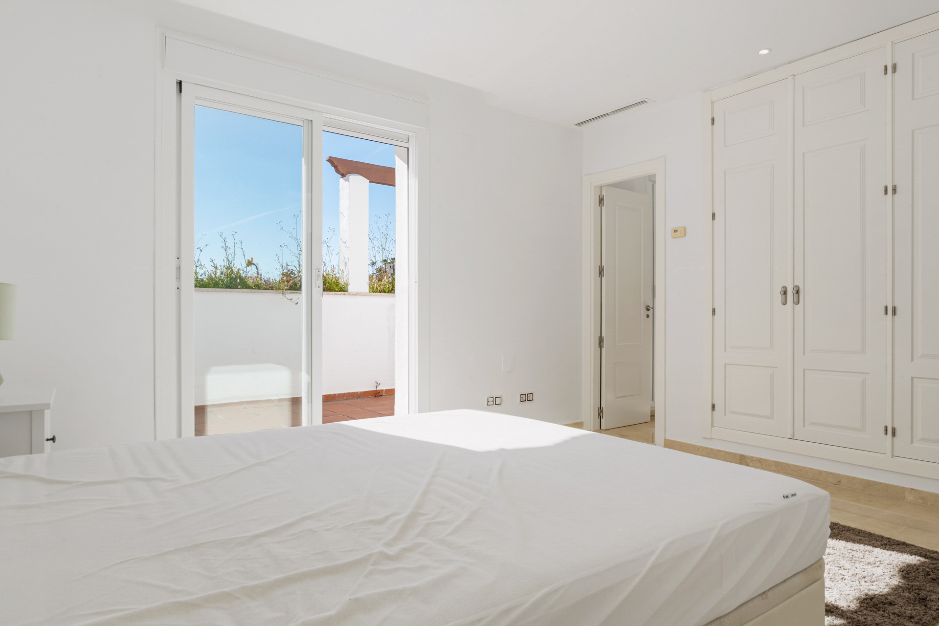 Bedroom with white walls, built-in wardrobe, and glass sliding doors opening to an outdoor terrace.