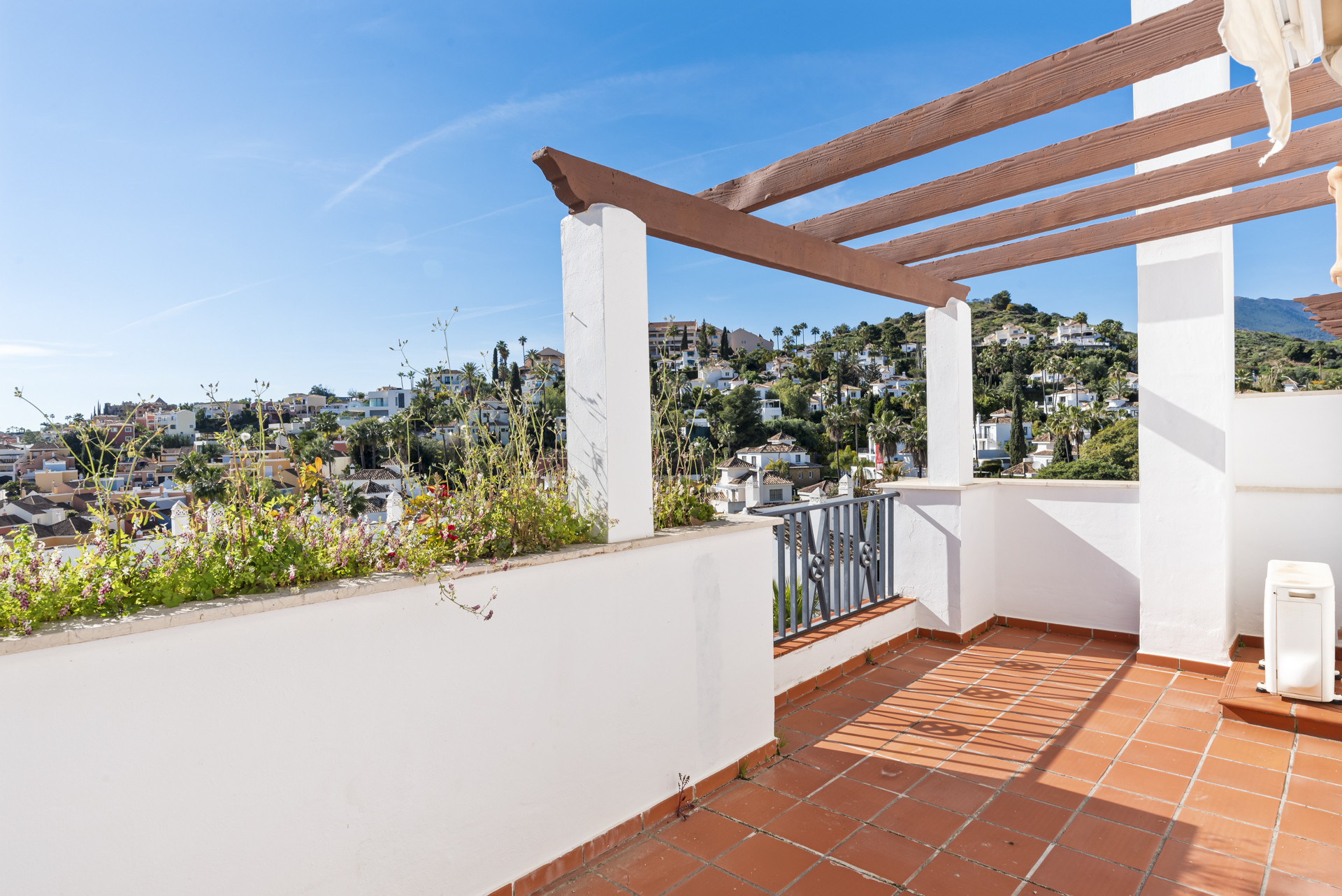 Terra cotta tiled terrace overlooking a white village on a hillside under a blue sky.