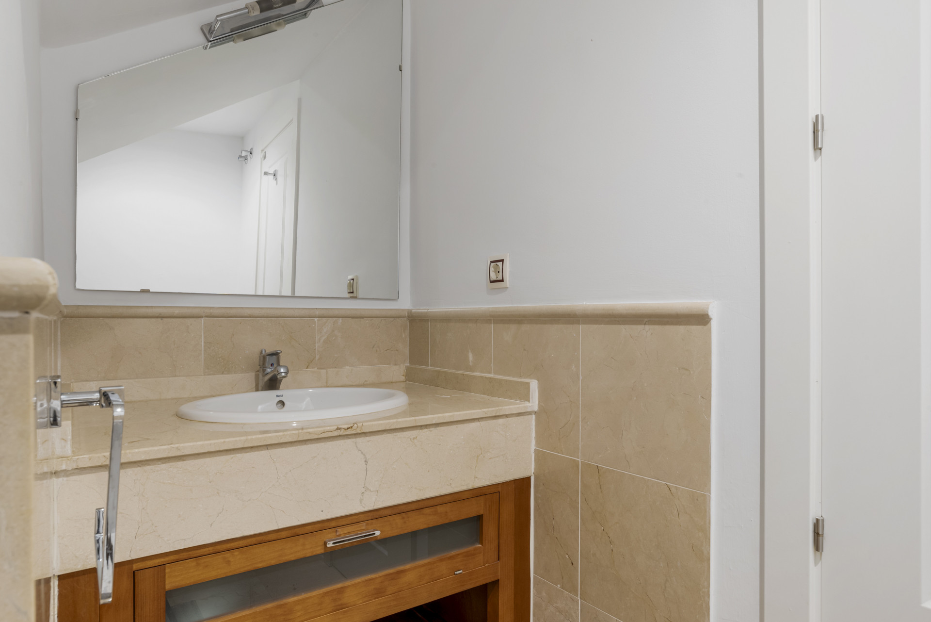 Bathroom vanity with a rectangular mirror, a white sink, and light-colored tiled countertop.