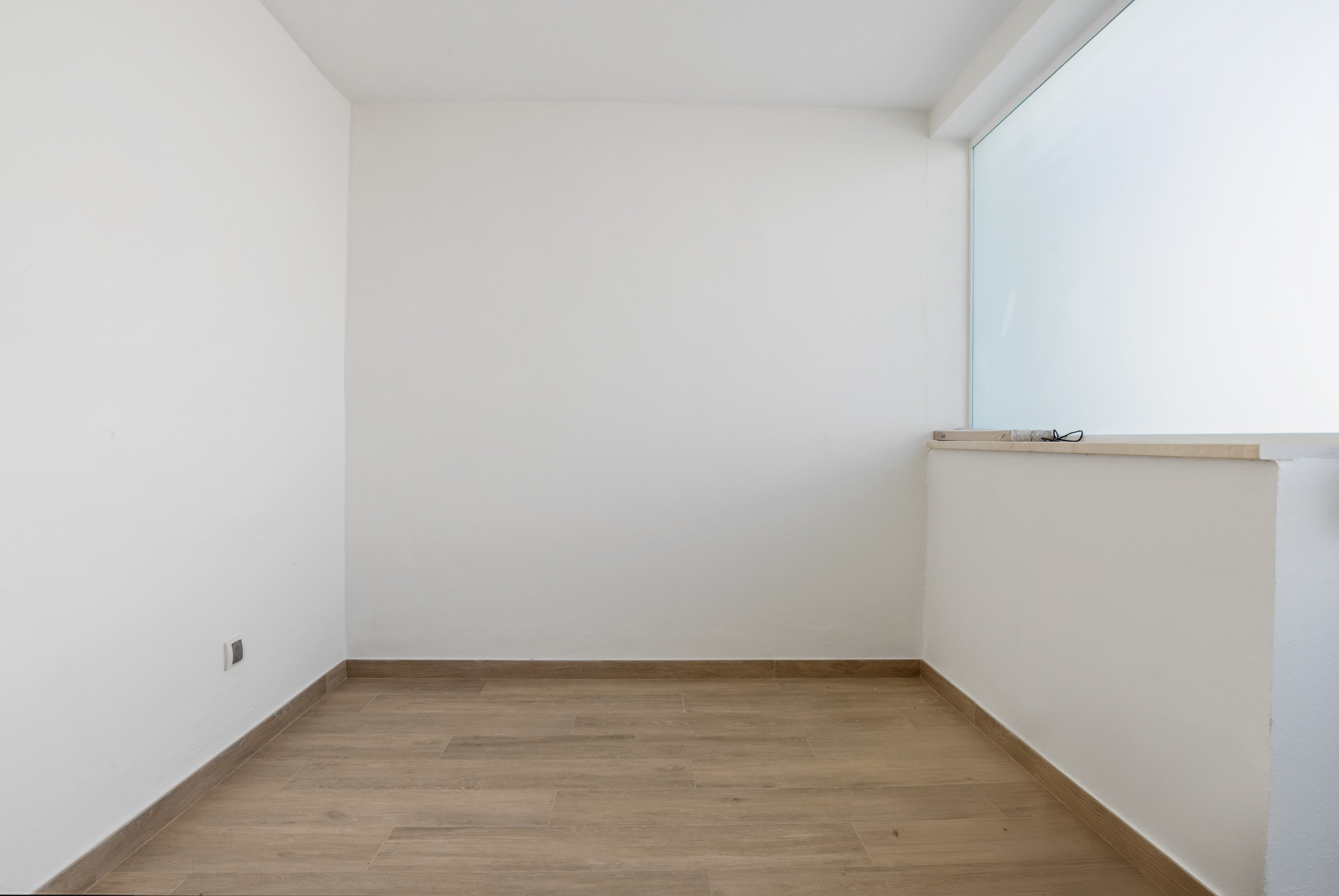 Empty room with light wood-effect flooring, white walls, and a large horizontal window.