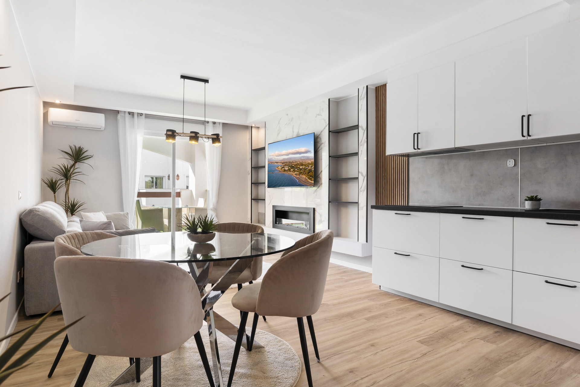 Open kitchen and dining area with glass table and modern decor, leading to outdoor space.