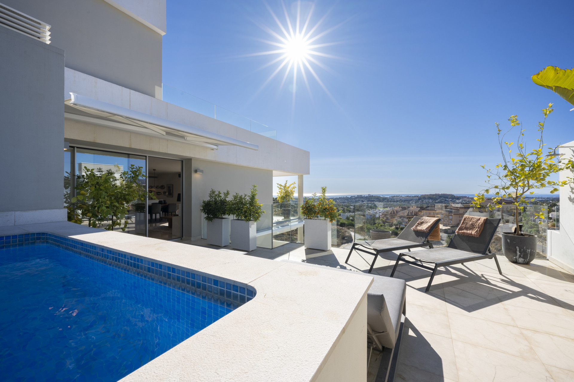 Sunlit terrace featuring loungers, a pool, and a scenic view of the landscape beyond.