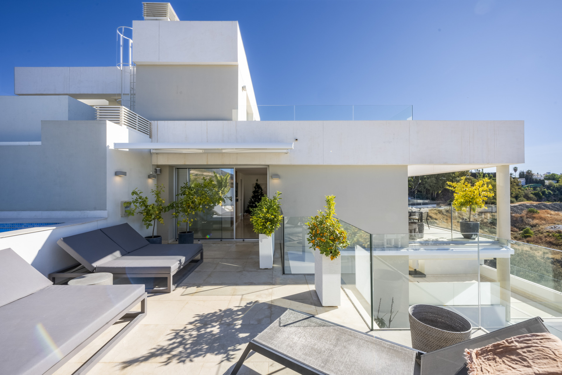 Contemporary outdoor space with loungers, glass railings, and a glimpse of the pool area.