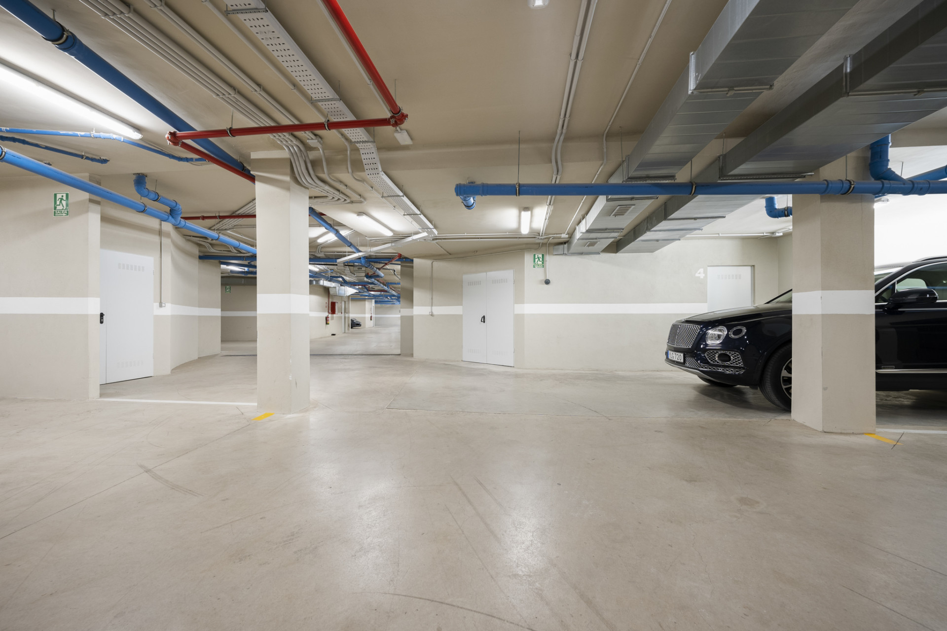 Underground parking area with visible vehicles and colorful pipes on the ceiling.