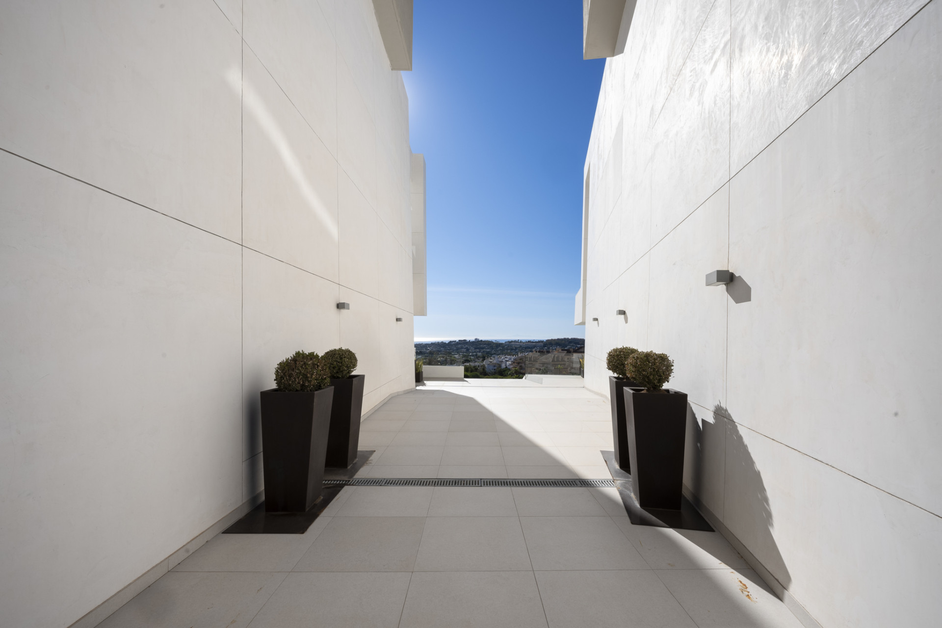 Narrow passageway between white walls leading to an open view.