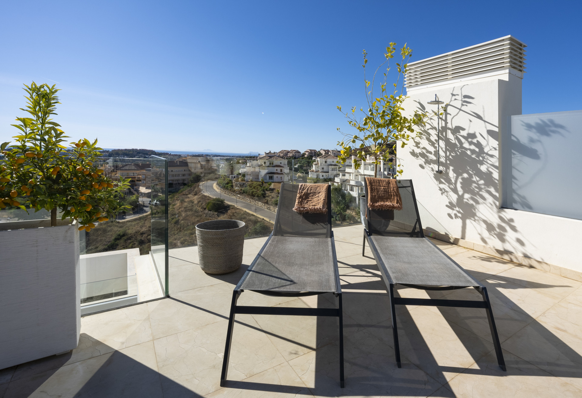 Sunny terrace with loungers and greenery overlooking a scenic view.