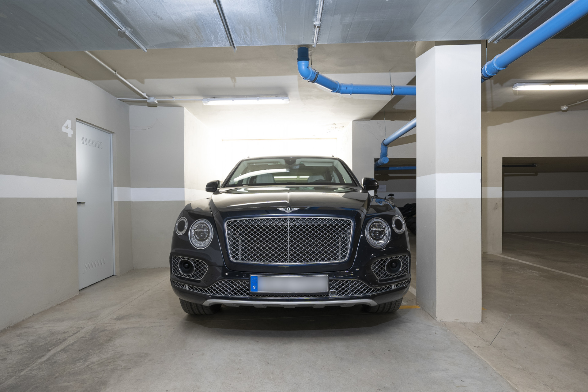 Luxury vehicle parked in an underground garage with clear space and structural elements.