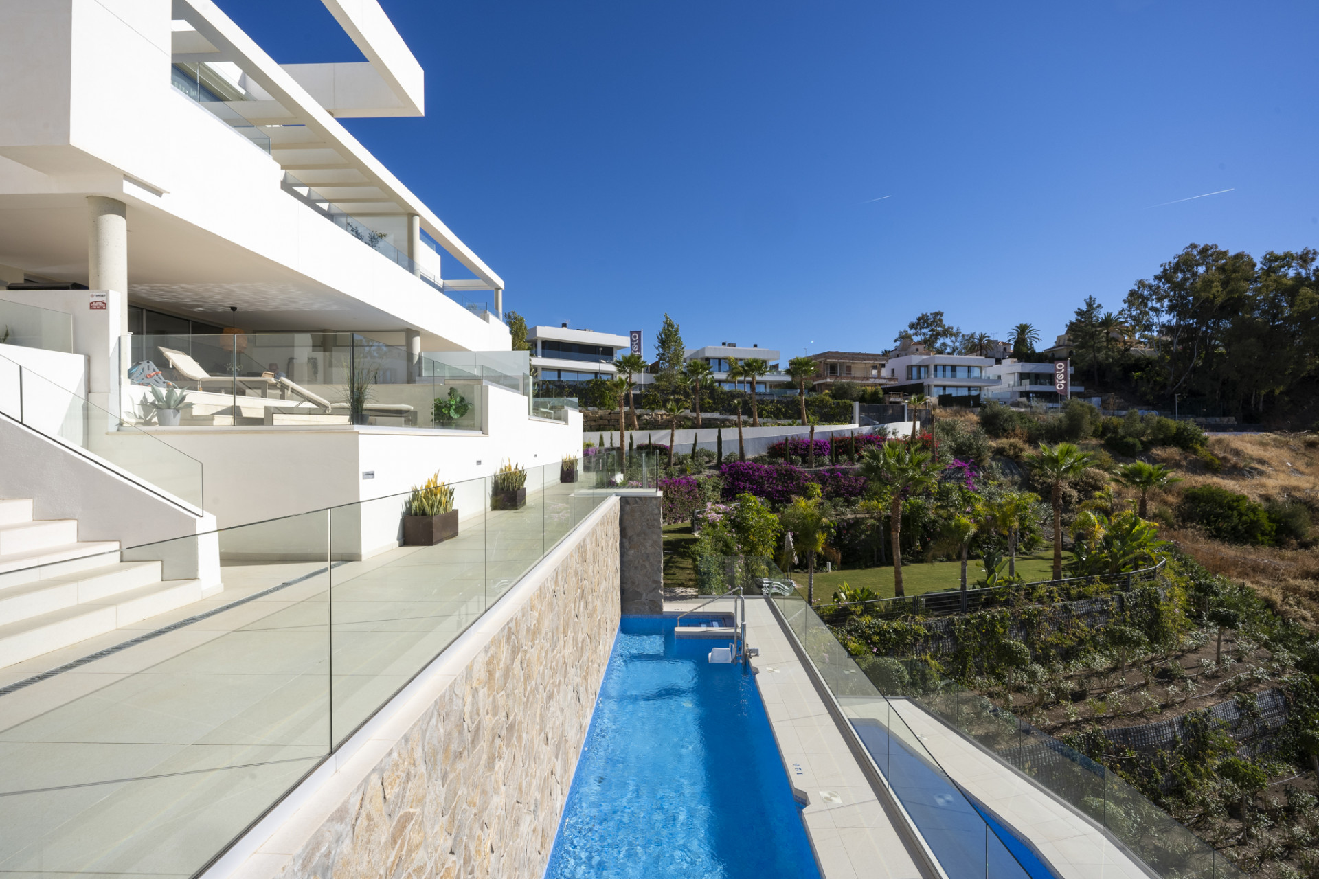 View of the poolside and landscaped gardens under a clear sky. Modern architecture visible.