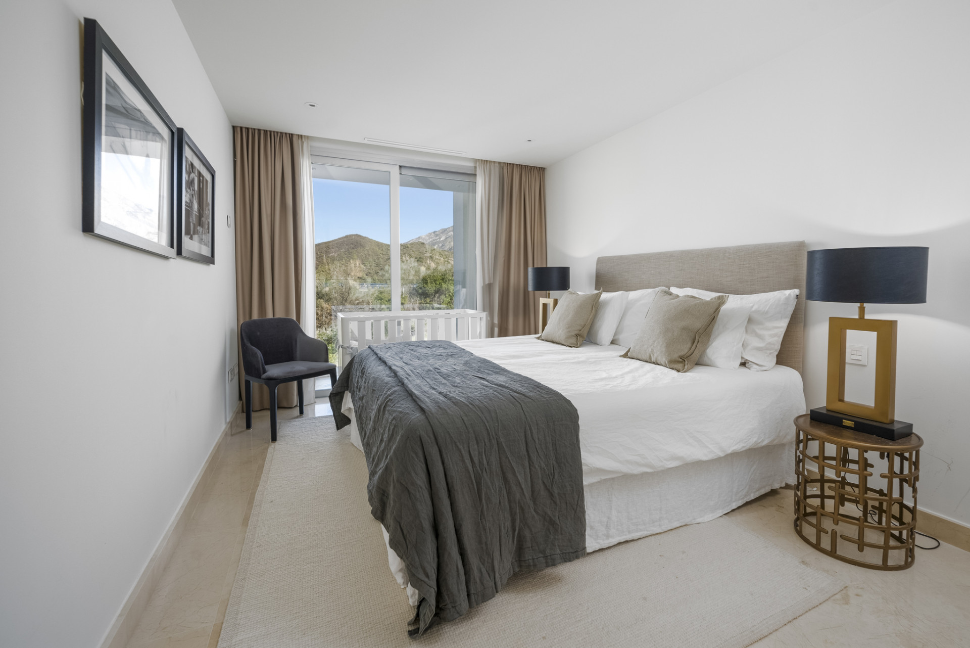 Bedroom featuring a double bed with view through large window and decorative armchair.