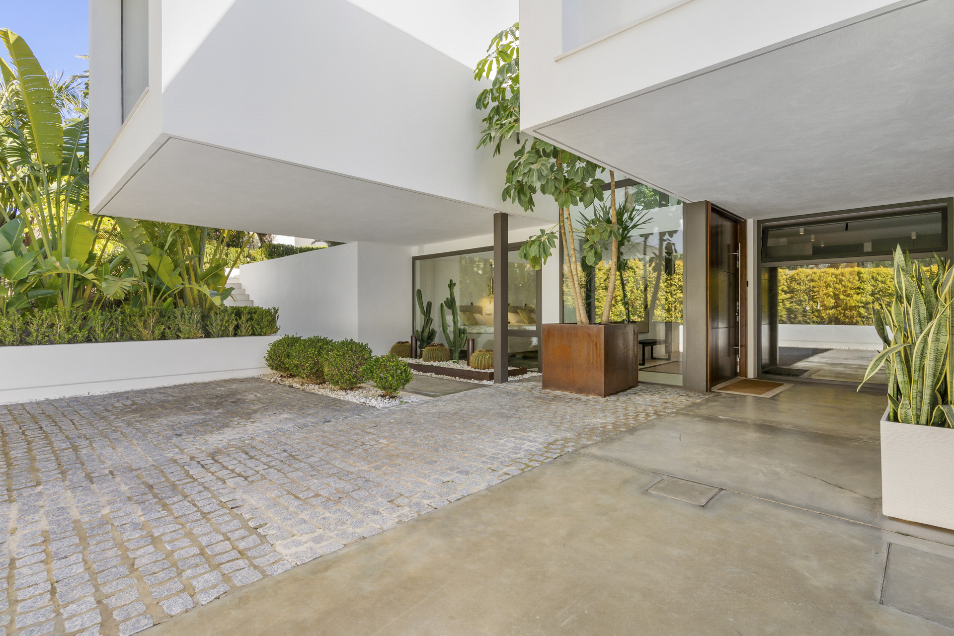 Modern building entrance with large planter boxes, stone path, and glass walls revealing interior plants.