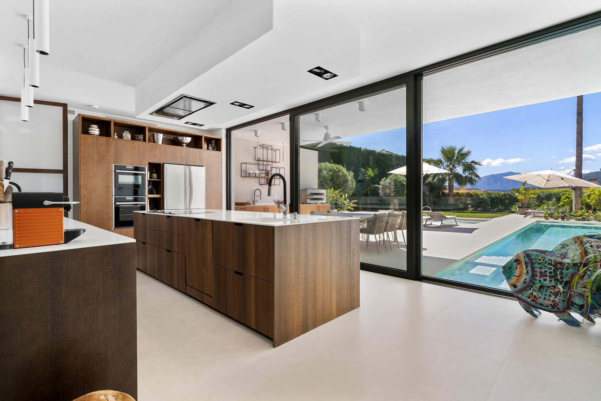 Modern kitchen with a large wooden island, integrated appliances, and sliding glass doors opening to a pool.
